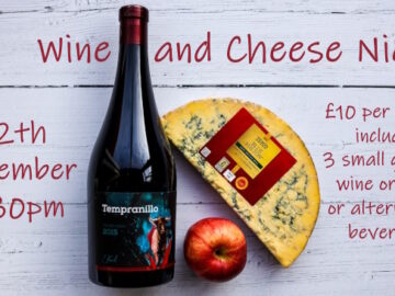 An unopened bottle of Italian red and a large half circle of blue cheese arranged with a red apple promotes the 12th December wine and cheese night.